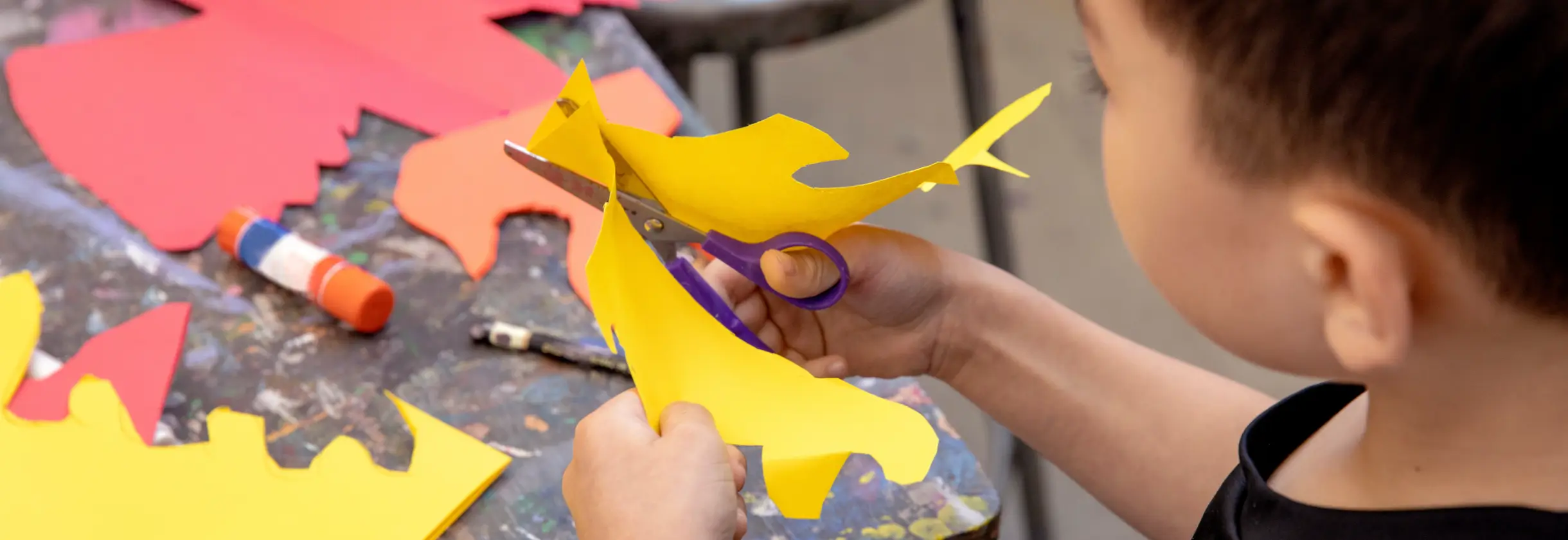 Student cutting a wavy pattern into yellow paper.