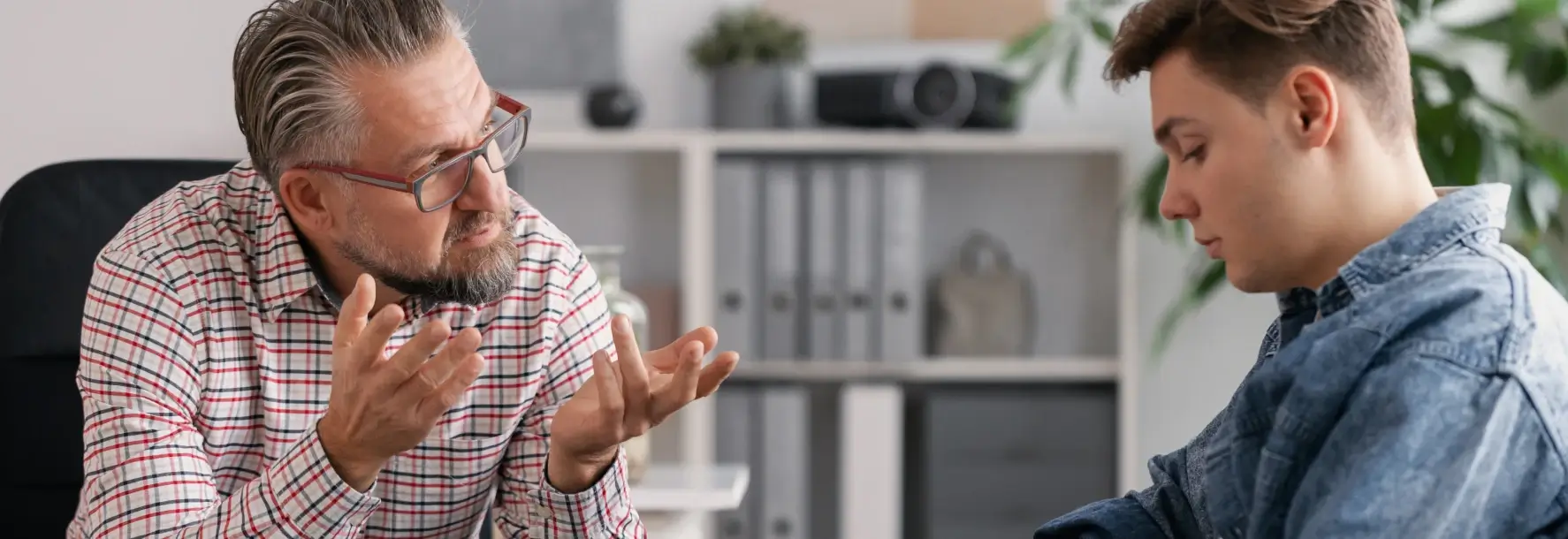 Middle-aged man speaking empathetically with a teenage boy during a one-on-one counseling session in an office setting.