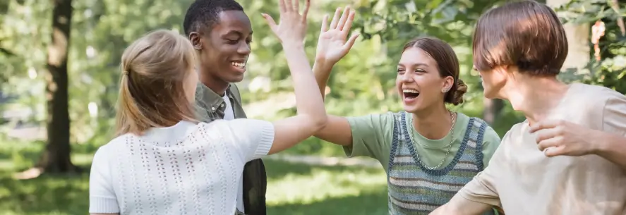 Four teen students smiling and high-fiving during summer.