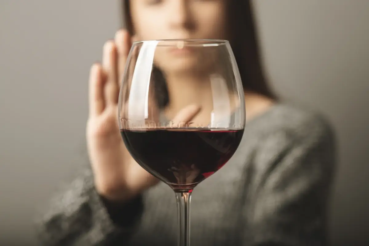 Young woman making a rejecting gesture with her hand toward a glass of red wine, symbolizing refusal or abstinence from alcohol.