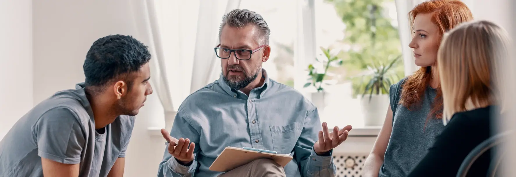 Therapist facilitating a group counseling session with three young participants seated in a circle, engaged in a serious conversation.
